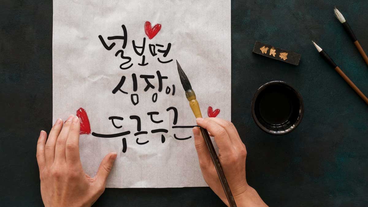 Gros plan sur les main d'une personne tenant un pinceau au dessus d'une feuille comportant une calligraphie  coréenne moderne