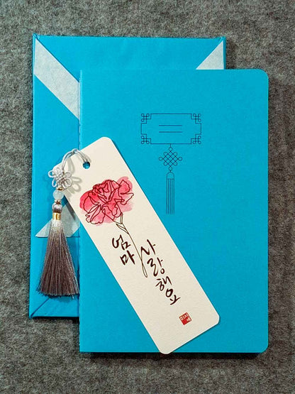 Marque page calligraphié "je t'aime maman" en coréen, avec un nœud coréen, un carnet décoré et un paquet cadeau plié en forme de hanbok. Le tout dans les tons bleu