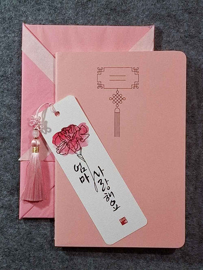 Marque page calligraphié "je t'aime maman" en coréen, avec un nœud coréen, un carnet décoré et un paquet cadeau plié en forme de hanbok. Le tout dans les tons rose pastel