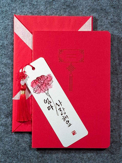 Marque page calligraphié "je t'aime maman" en coréen, avec un nœud coréen, un carnet décoré et un paquet cadeau plié en forme de hanbok. Le tout dans les tons rouge