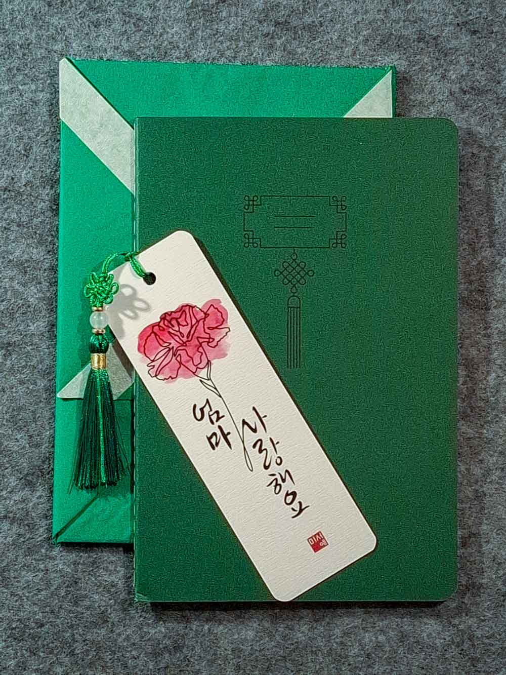 Marque page calligraphié "je t'aime maman" en coréen, avec un nœud coréen, un carnet décoré et un paquet cadeau plié en forme de hanbok. Le tout dans les tons vert sapin