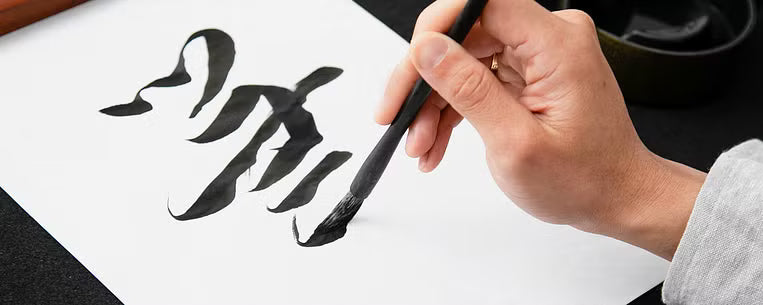 Photo gros plan d'une main calligraphiant en noir un caractère chinois avec un pinceau sur une feuille blanche